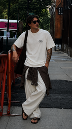 male model standing in city setting wearing oversized cream graphic t shirt with chest typography print relaxed fit streetwear fashion