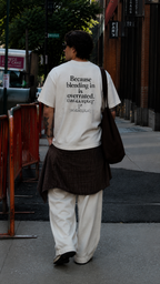 male model viewed from behind wearing oversized cream graphic t shirt featuring bold statement back graphic relaxed fit streetwear fashion