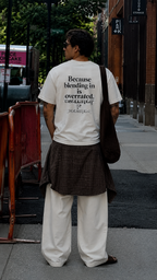 back view of male model wearing oversized off white graphic t shirt with large because blending in is overrated graphic print urban streetwear outfit