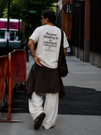 male model walking away wearing oversized off white graphic t shirt with oversized typography back print urban streetwear style