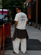 male model looking over shoulder wearing oversized cream graphic t shirt showcasing large statement graphic on back streetwear fashion