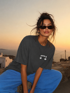 Woman sitting on stone wall wearing oversized charcoal graphic t-shirt front view with relaxed fit, urban streetwear fashion at sunset