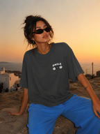 Woman sitting on stone wall wearing oversized charcoal graphic t-shirt front view with small chest graphic, urban graphic streetwear