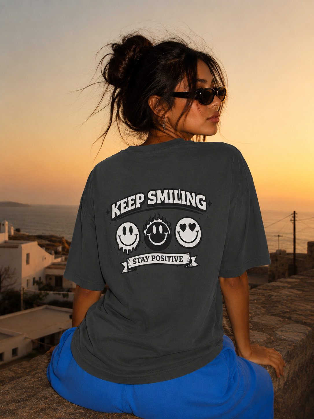 Woman sitting back view wearing oversized charcoal graphic t-shirt with large Keep Smiling graphic print, oversized streetwear fashion