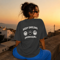 Woman sitting wearing oversized charcoal graphic t-shirt back view showing large Keep Smiling graphic design, urban streetwear outfit