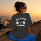 Woman sitting wearing oversized charcoal graphic t-shirt back view showing large Keep Smiling graphic design, urban streetwear outfit