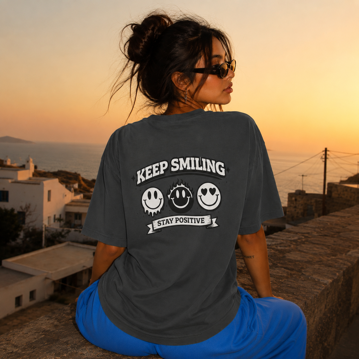 Woman sitting wearing oversized charcoal graphic t-shirt back view showing large Keep Smiling graphic design, urban streetwear outfit