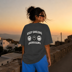 Woman standing back view wearing oversized charcoal graphic t-shirt displaying large Keep Smiling graphic print, urban graphic streetwear
