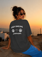 Woman seated back view wearing oversized charcoal graphic t-shirt featuring Keep Smiling graphic print, modern streetwear fashion