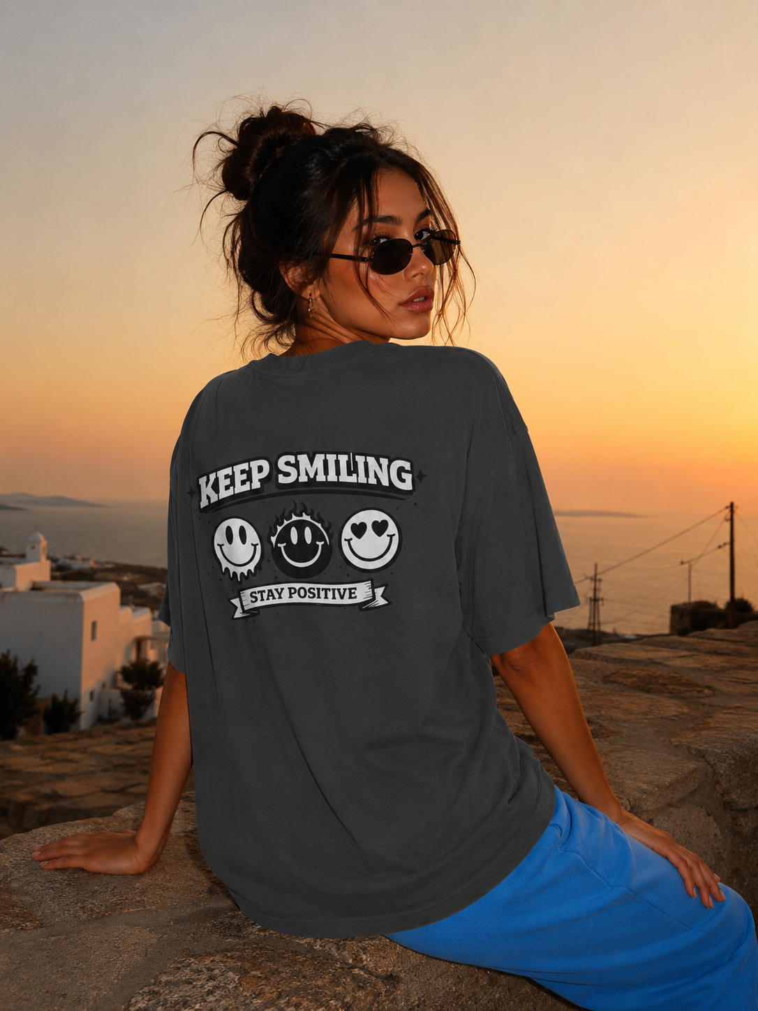 Woman seated back view wearing oversized charcoal graphic t-shirt featuring Keep Smiling graphic print, modern streetwear fashion