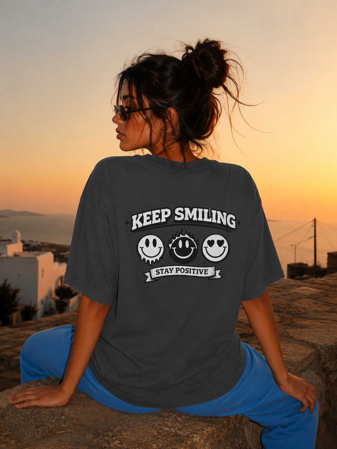 Woman sitting on stone wall wearing oversized charcoal graphic t-shirt back view with large graphic print, relaxed urban streetwear outfit