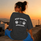 Woman sitting sideways wearing oversized charcoal graphic t-shirt back view displaying Keep Smiling graphic design, charcoal streetwear fashion
