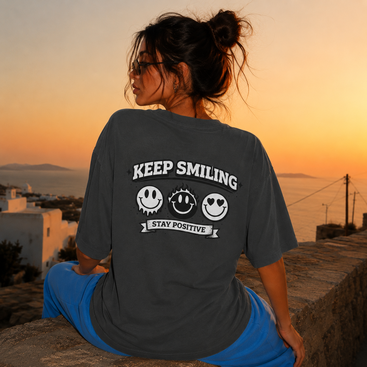 Woman sitting sideways wearing oversized charcoal graphic t-shirt back view displaying Keep Smiling graphic design, charcoal streetwear fashion