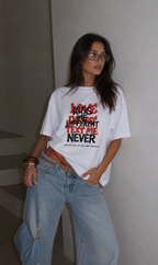 Woman standing with denim shoulder bag wearing oversized white graphic t-shirt front view featuring Kiss Me Different Text Me Never graphic, modern streetwear fashion