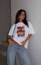 Woman posing with hands in pockets wearing oversized white graphic t-shirt front graphic print, relaxed fit urban graphic streetwear look