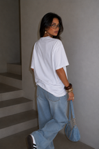 Woman walking away wearing oversized white graphic t-shirt back view with clean white back and relaxed fit, minimalist streetwear outfit