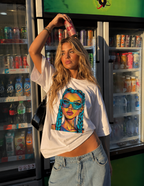 Woman holding soda can above her head wearing oversized white graphic t-shirt front view with colorful braided girl artwork, relaxed urban streetwear outfit