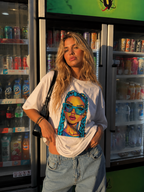 Woman adjusting oversized white graphic t-shirt with colorful braided girl graphic front view, casual streetwear fashion inside convenience store