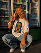 Woman squatting while holding soda can wearing oversized white graphic t-shirt front graphic featuring colorful braided girl illustration, oversized urban streetwear outfit
