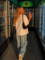 Woman walking through convenience store wearing oversized white graphic t-shirt back view with clean white back, minimalist oversized streetwear outfit