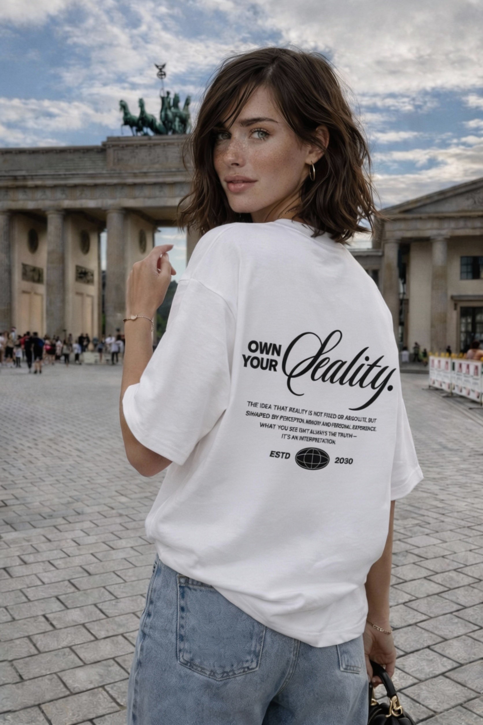 female model over shoulder pose wearing oversized white graphic streetwear t shirt own your reality back print urban streetwear outfit