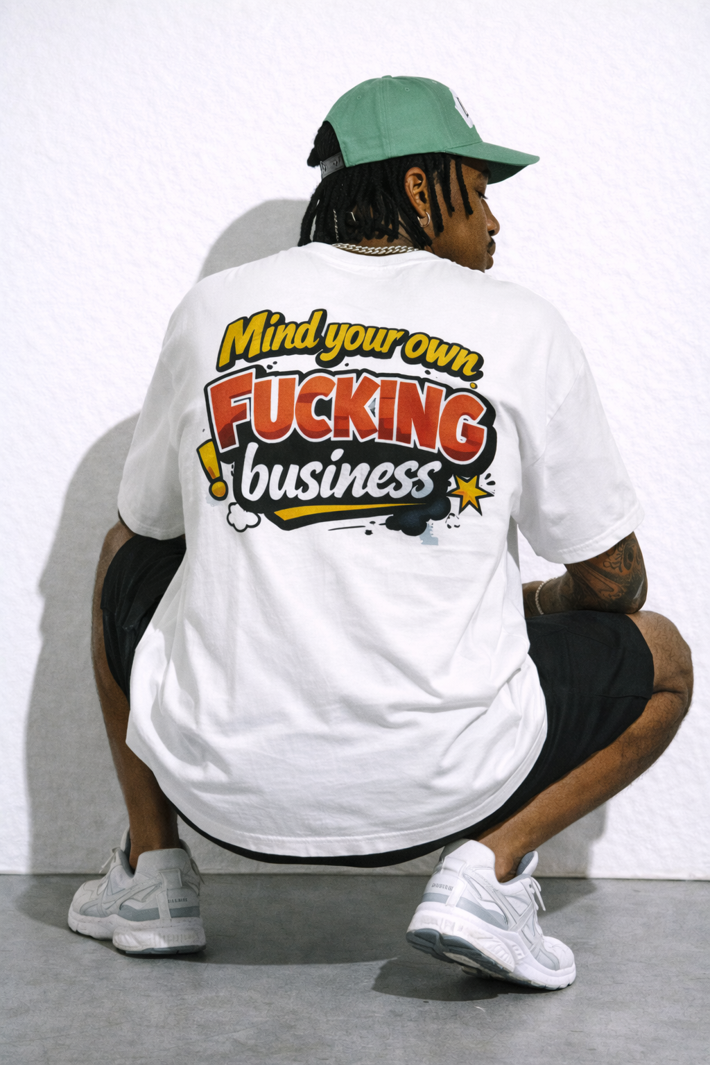 male model seated back pose wearing oversized white graphic streetwear t shirt mind your own fucking business graphic design urban streetwear outfit