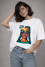 Female model in white oversized “Bold Looks Good” graphic t-shirt featuring vibrant illustrated portrait design, paired with denim jeans, trendy women’s streetwear fashion.