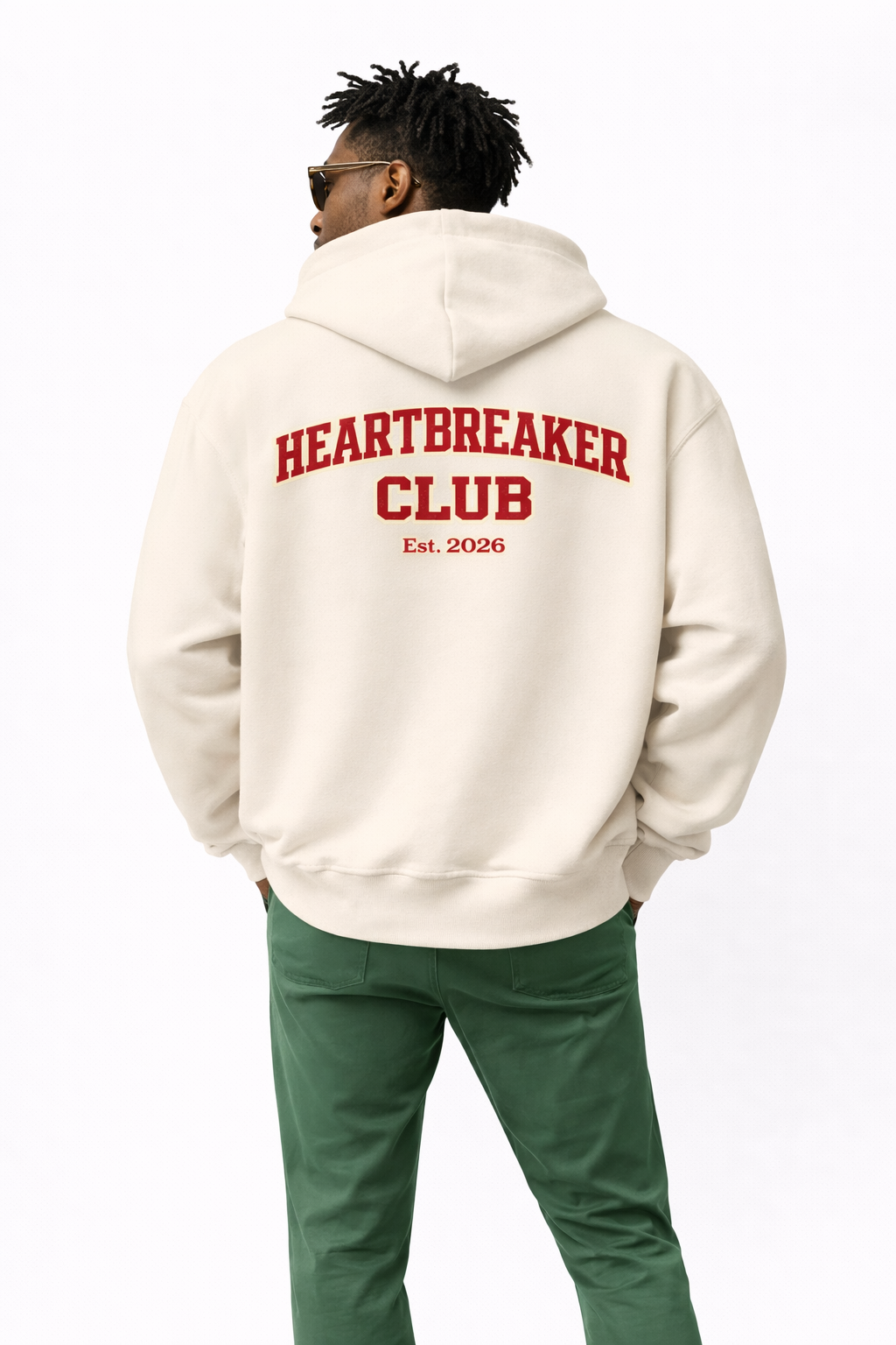 Man wearing beige oversized “Heartbreaker Club” hoodie with red back graphic print, relaxed streetwear style.