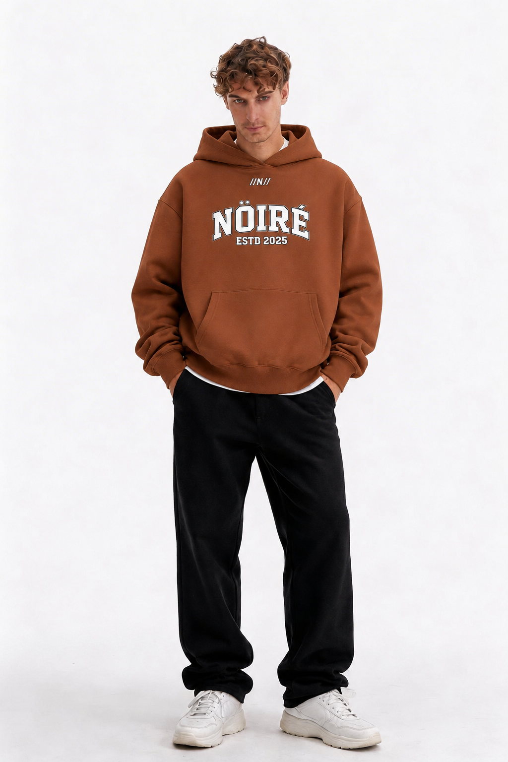 Male model wearing brown oversized Nöiré ESTB 2025 graphic hoodie, full-body front view, urban streetwear outfit