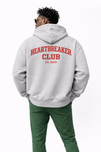 Man wearing grey oversized “Heartbreaker Club” hoodie with red back graphic print, relaxed streetwear style.