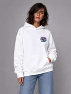female model relaxed pose wearing oversized white hoodie with small chest graphic urban streetwear outfit