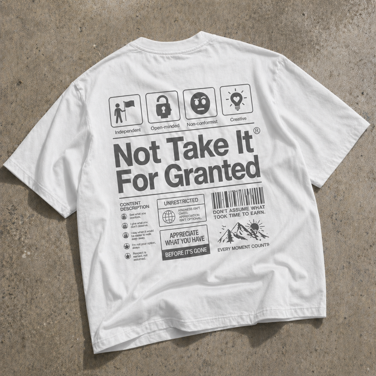 back view oversized white graphic t-shirt with grey “Not Take It For Granted” statement design laid flat on concrete background graphic streetwear