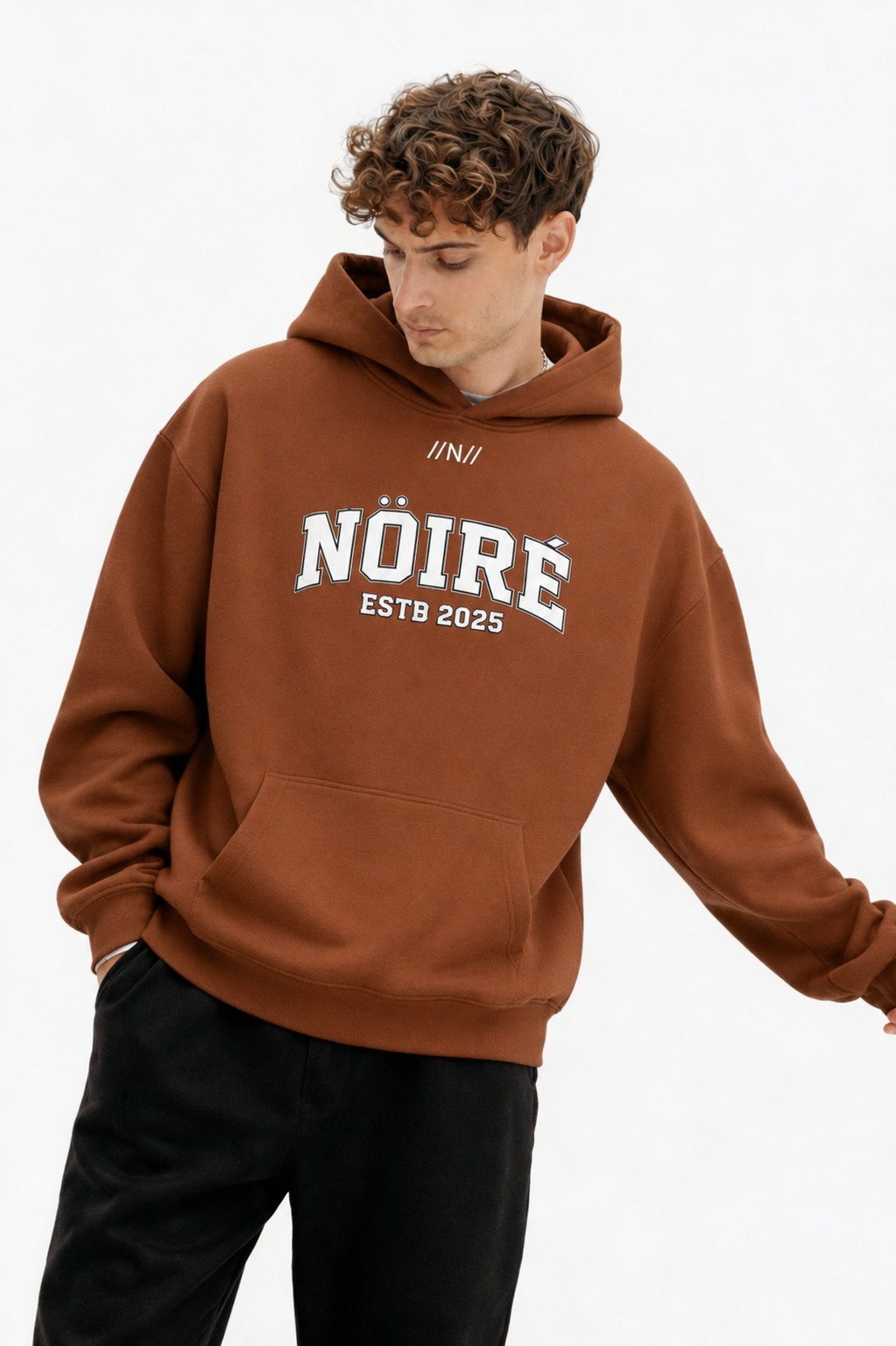 Male model wearing brown oversized Nöiré ESTB 2025 logo hoodie, close-up front view, streetwear fashion