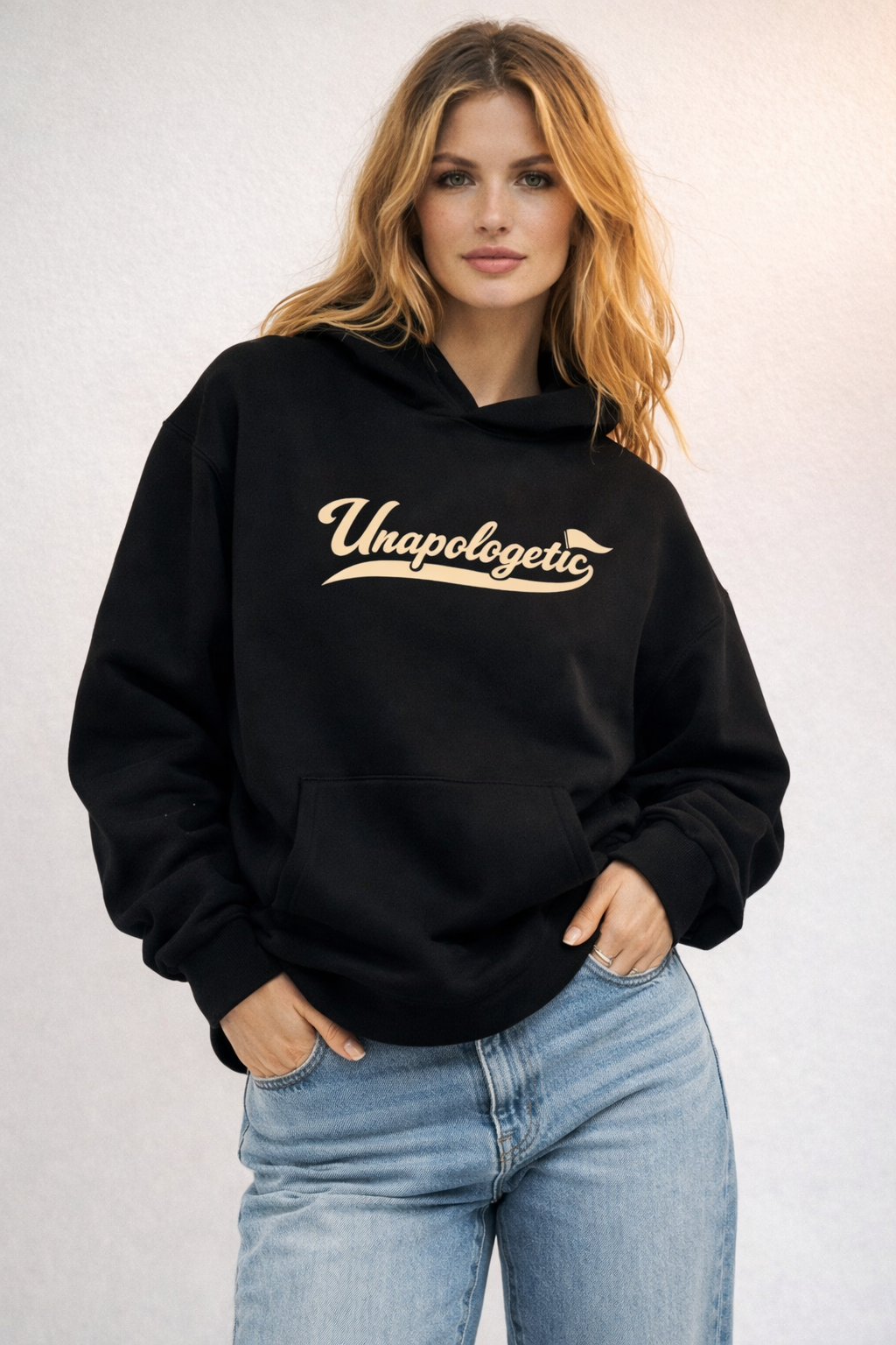 Noiré black oversized streetwear hoodie front view with “Unapologetic” script graphic in beige, worn by female model, unisex statement hoodie.