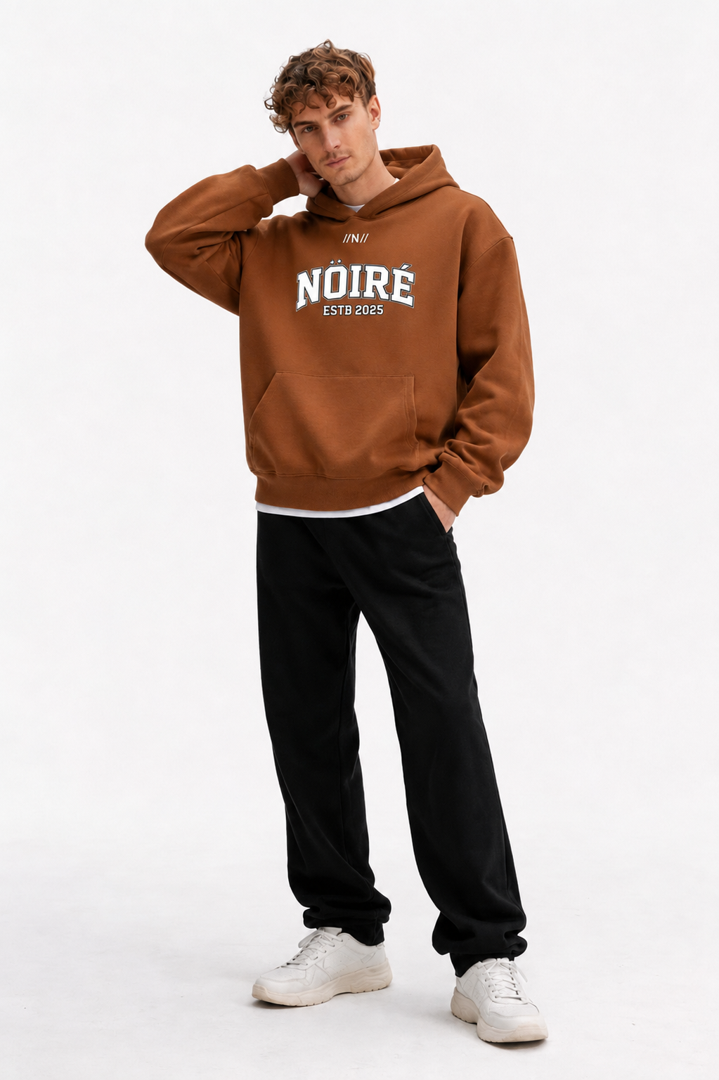 Male model posing in brown oversized Nöiré collegiate logo hoodie, front view, graphic streetwear