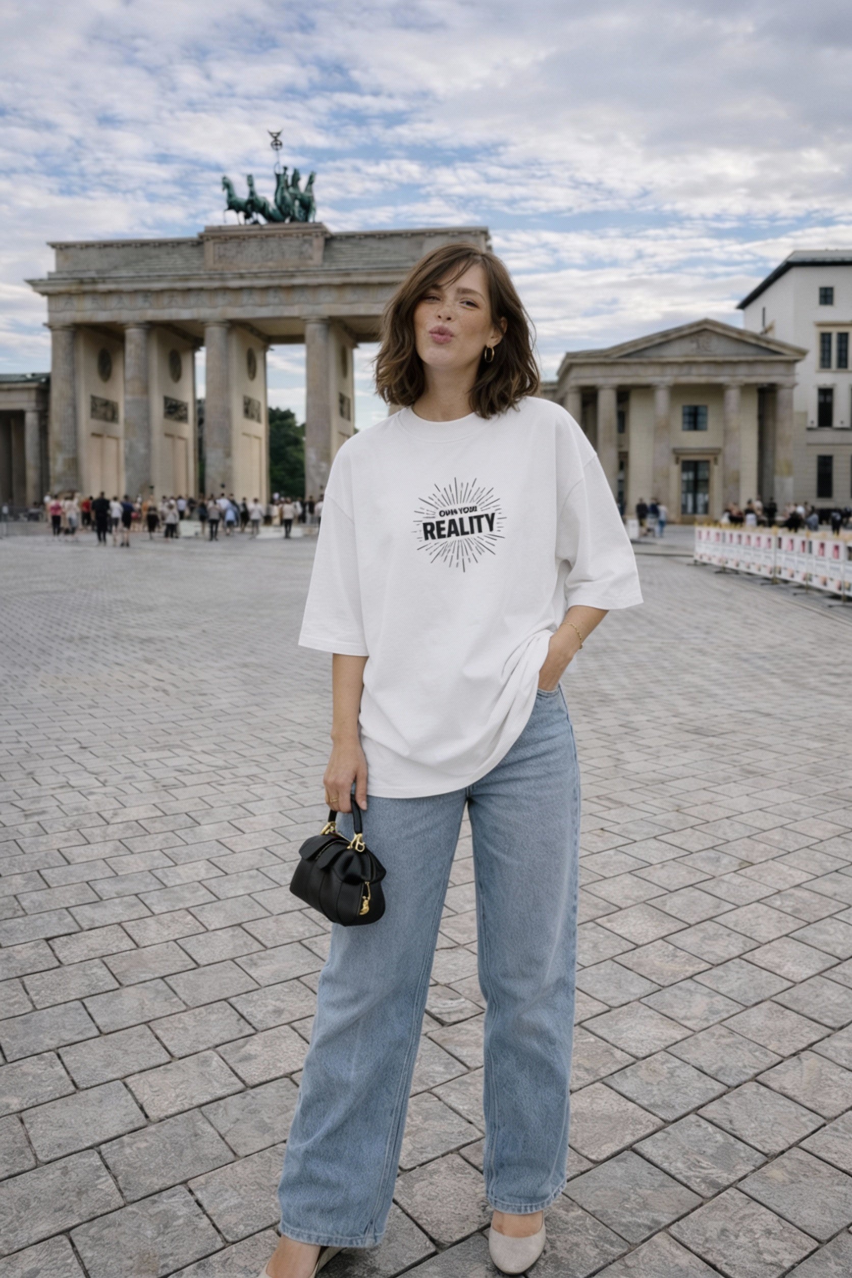 female model relaxed pose wearing oversized white graphic streetwear t shirt own your reality minimal typography design urban outfit