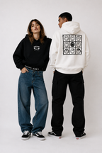 female model front pose wearing cropped black oversized hoodie with small chest graphic urban streetwear outfit while male model back view wearing off white oversized hoodie with smiley grid back print graphic streetwear fashion