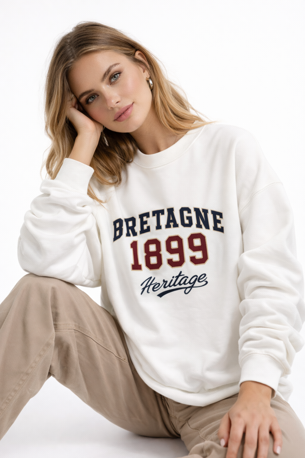 Female model sitting in cream oversized “Bretagne 1899 Heritage” sweatshirt featuring vintage collegiate typography, modern women’s casual outfit.
