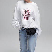 Model wearing white graphic sweatshirt with “Good Luck Without Me” typography, minimalist lifestyle studio photo