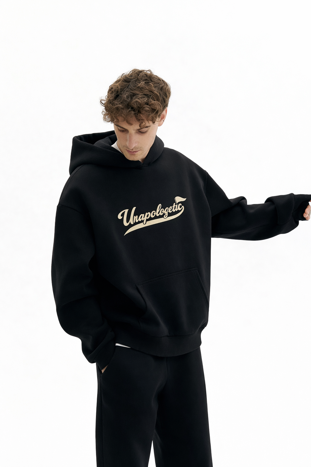 Noiré black oversized streetwear hoodie front view with “Unapologetic” script graphic in beige, worn by male model, unisex statement hoodie.