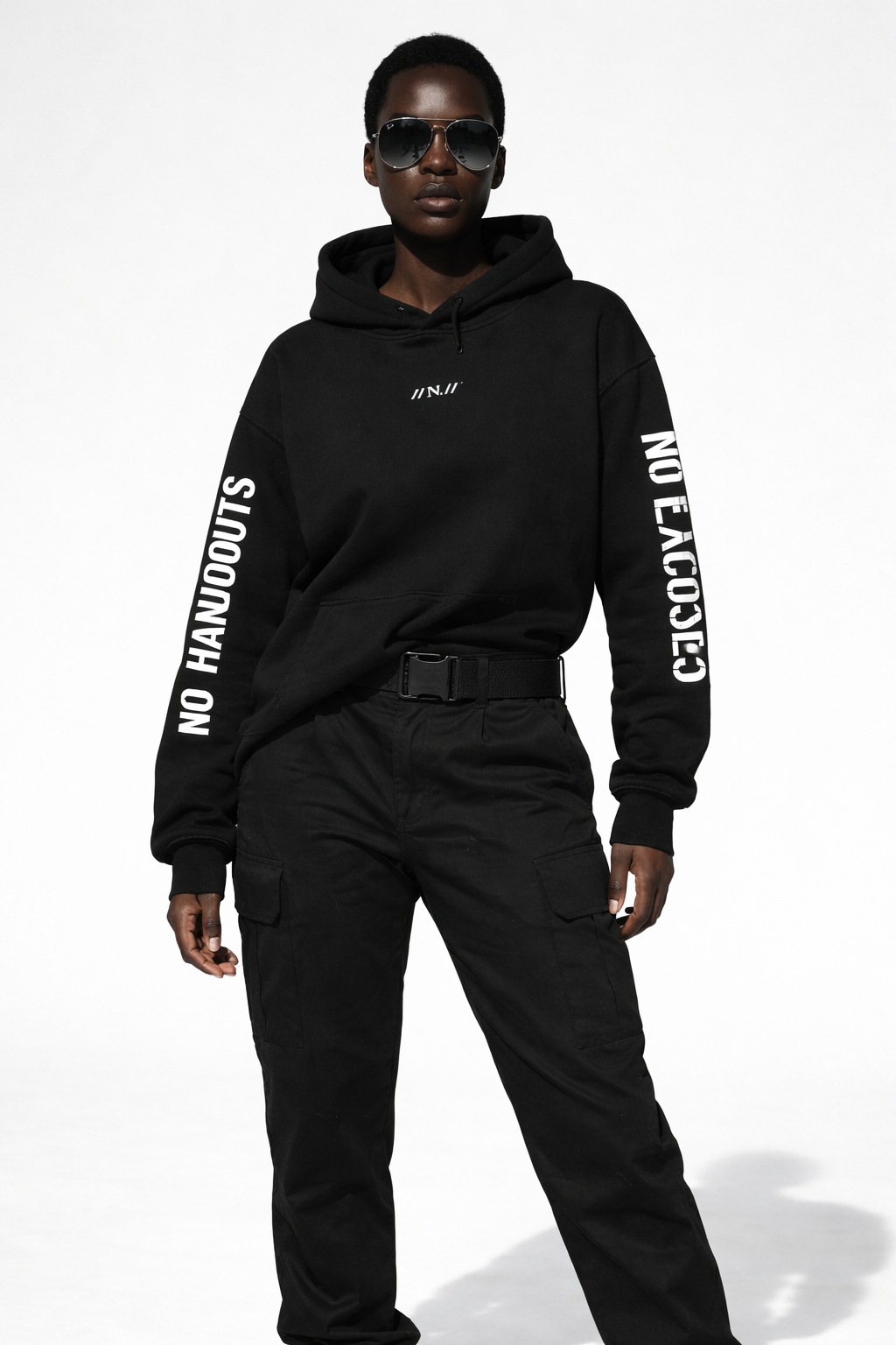 Female model wearing black oversized hoodie with “//N.//” chest logo and “NO HANDOUTS” and “NO EXCUSES” printed on sleeves, front full-body studio shot.