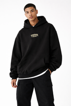 Male model in black oversized streetwear hoodie with minimalist chest detail, relaxed fit, studio setting.