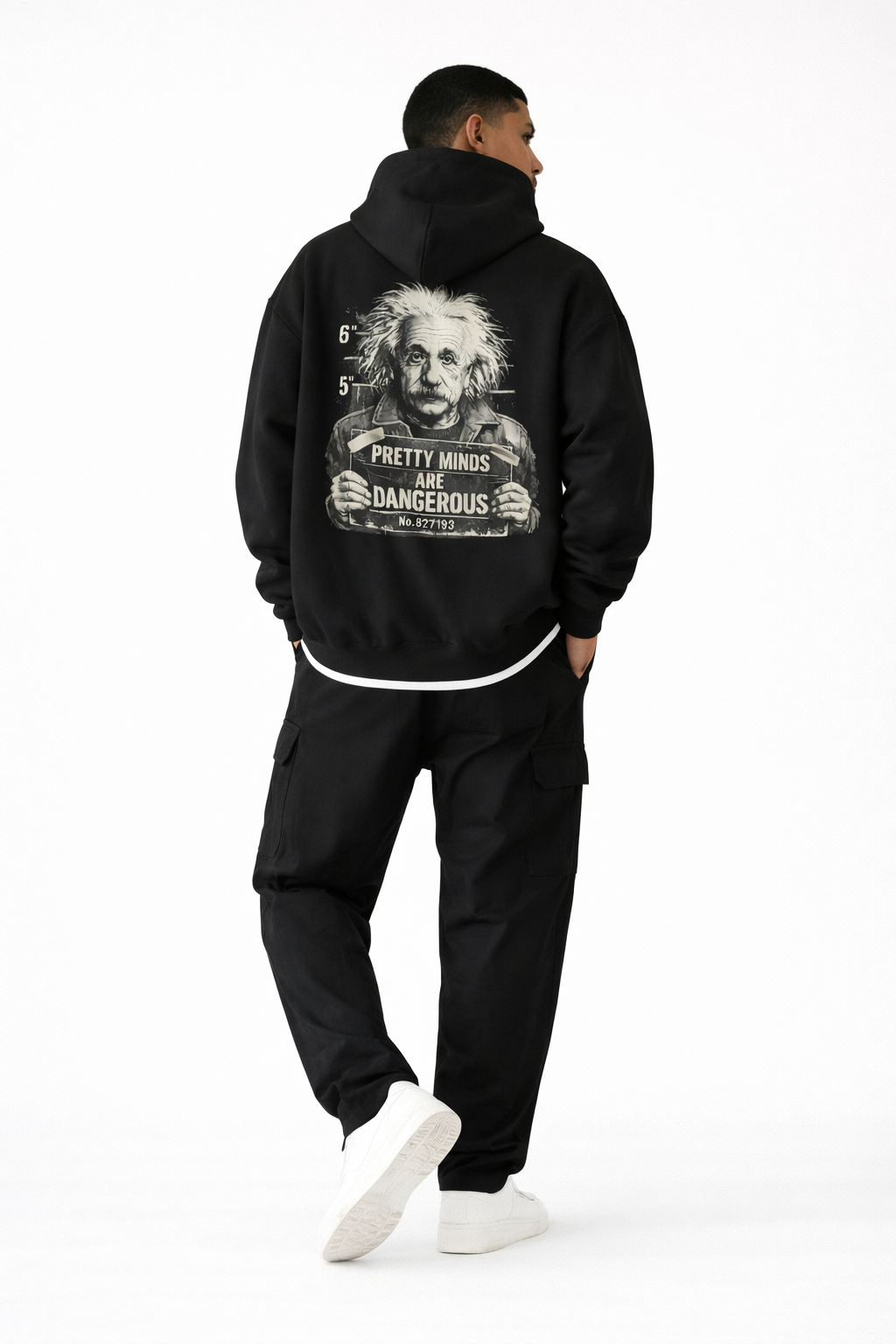 Full-body back view of male model in black oversized hoodie with large illustrated back print, black pants and sneakers, studio background.