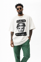 Beige oversized streetwear t-shirt “Fake it til you make it” with broken mask graphic print, male model wearing green pants, minimalist studio fashion photo