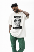 Beige graphic oversized t-shirt “Fake it til you make it” artistic mask illustration, male streetwear model with sunglasses and green trousers, clean white studio background