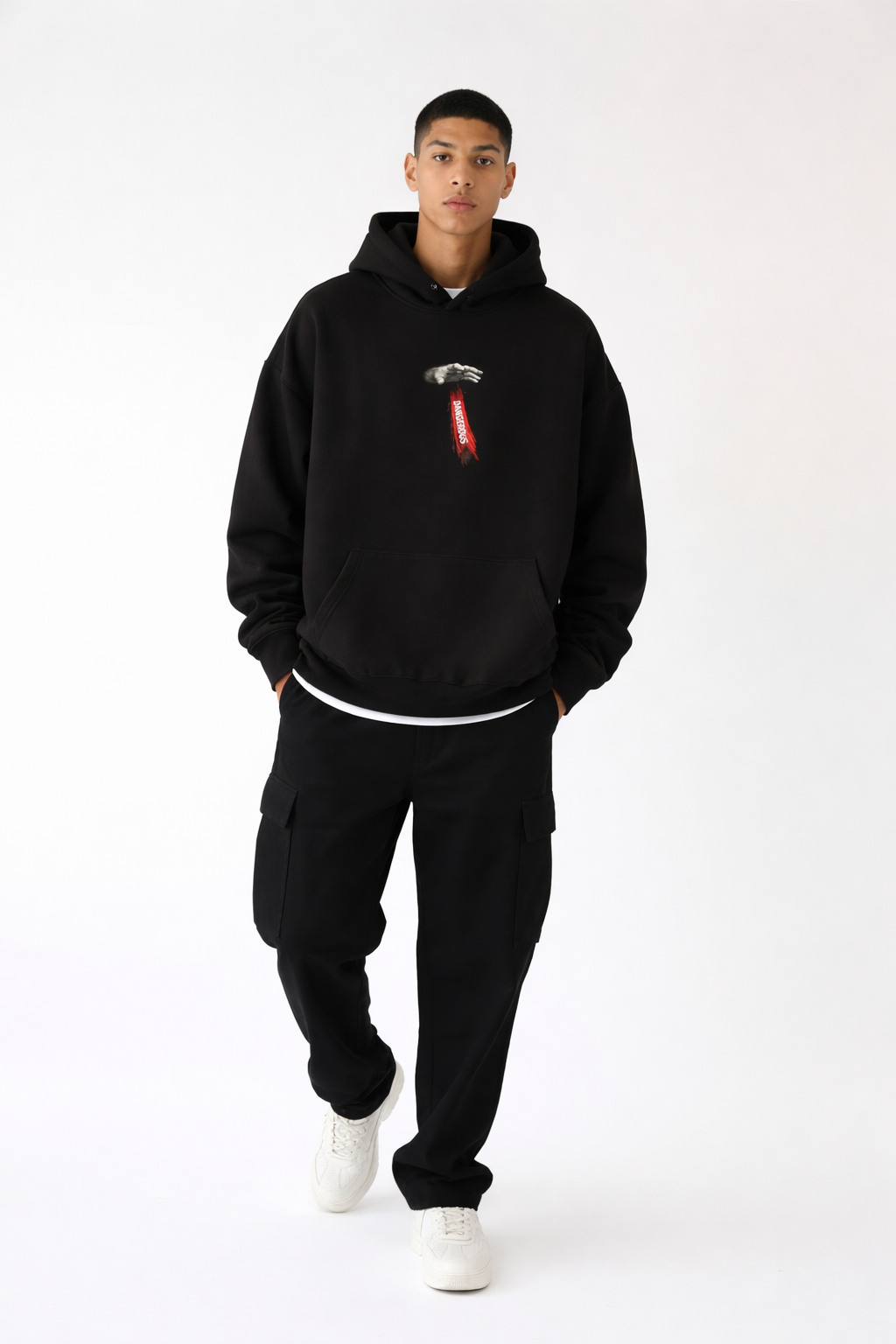Black streetwear hoodie front view with small red and white chest graphic, male model wearing black cargo pants and white sneakers, modern urban fashion