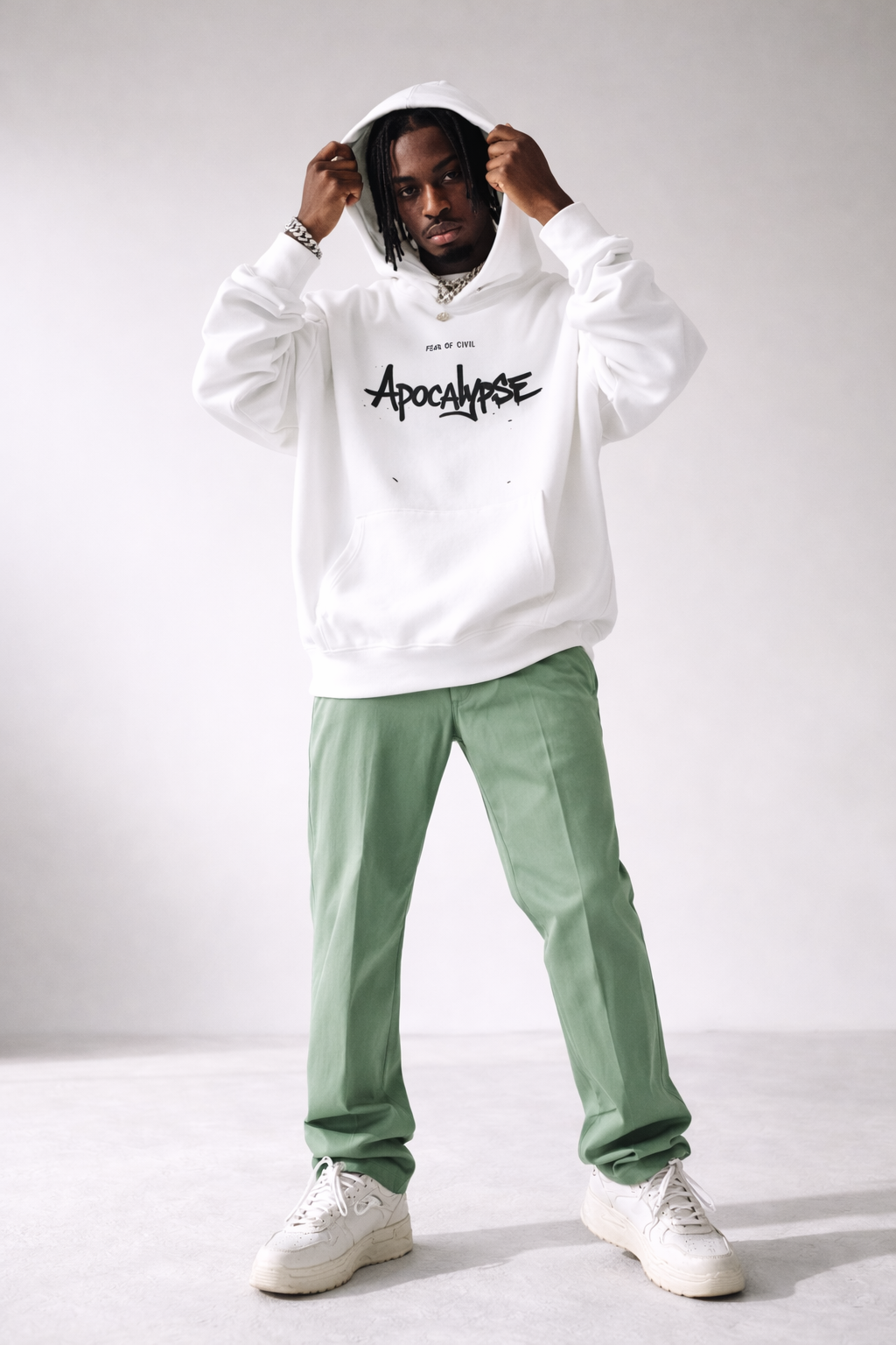 Men’s white oversized hoodie with “Apocalypse” graphic print on the front, modern streetwear sweatshirt styled with green pants, fashion product image.