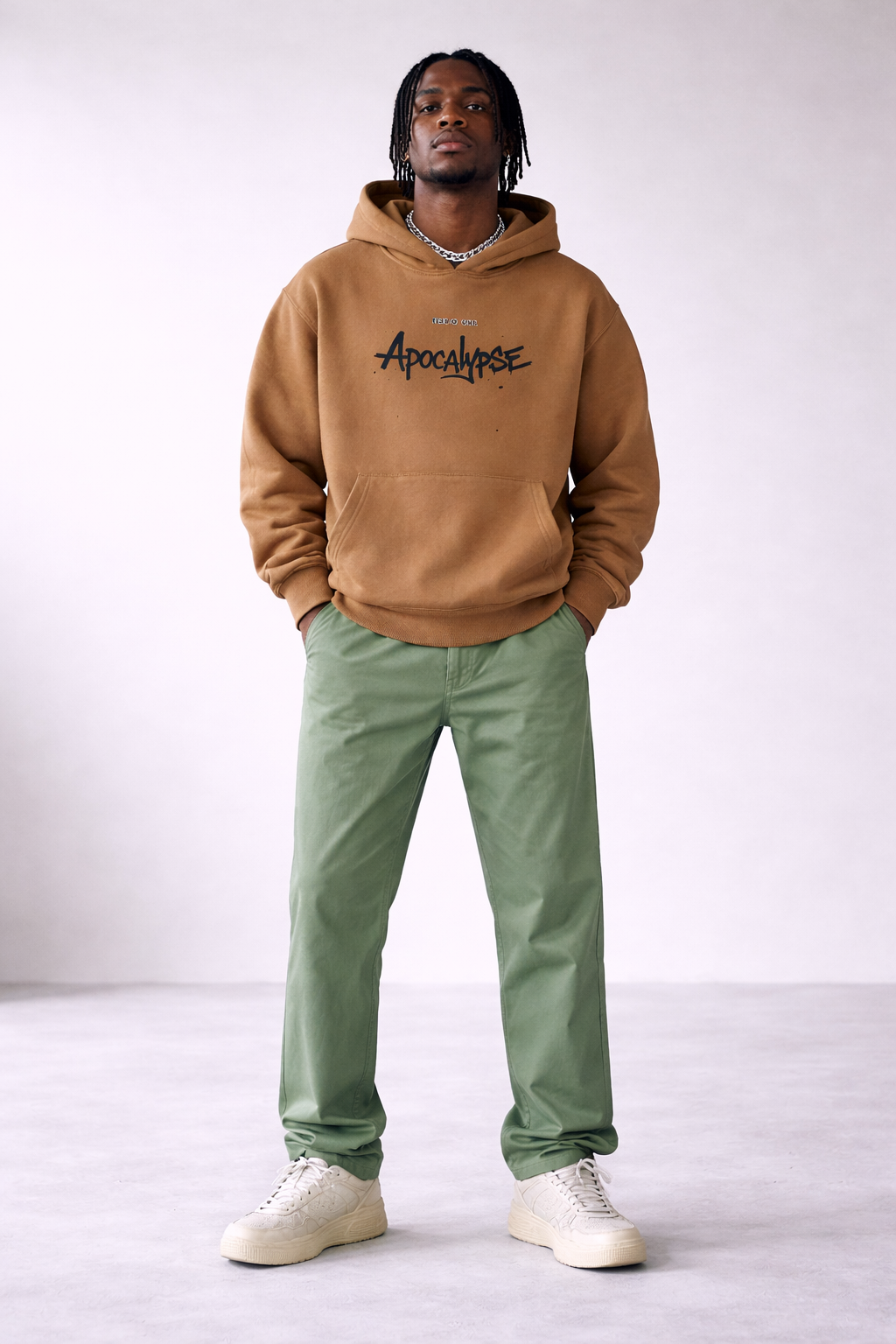 Men’s camel brown oversized hoodie with “Apocalypse” front graphic print, contemporary streetwear sweatshirt styled with green trousers, product image.