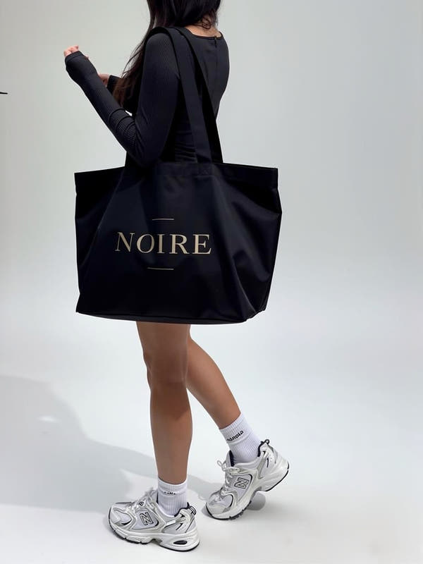 Model wearing Noiré logo statement canvas tote bag black streetwear full body view