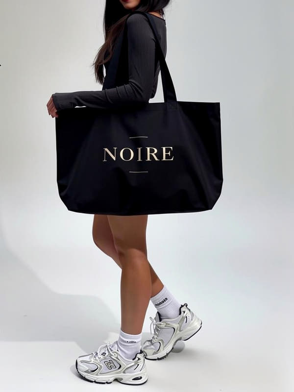 Woman carrying Noiré logo statement canvas tote bag black lifestyle side view